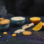 Horizontal photo of cookies and oatmeal in bowls, Half cut and sliced orang eon ground. High quality photo